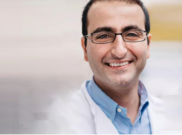 Fußspezialist Dr. Michel Chraim von vorne, er lacht und trägt eine Brille, ein hellblaues Hemd und ein weisses Arztgewand, man sieht den Kopf und den Oberkörper